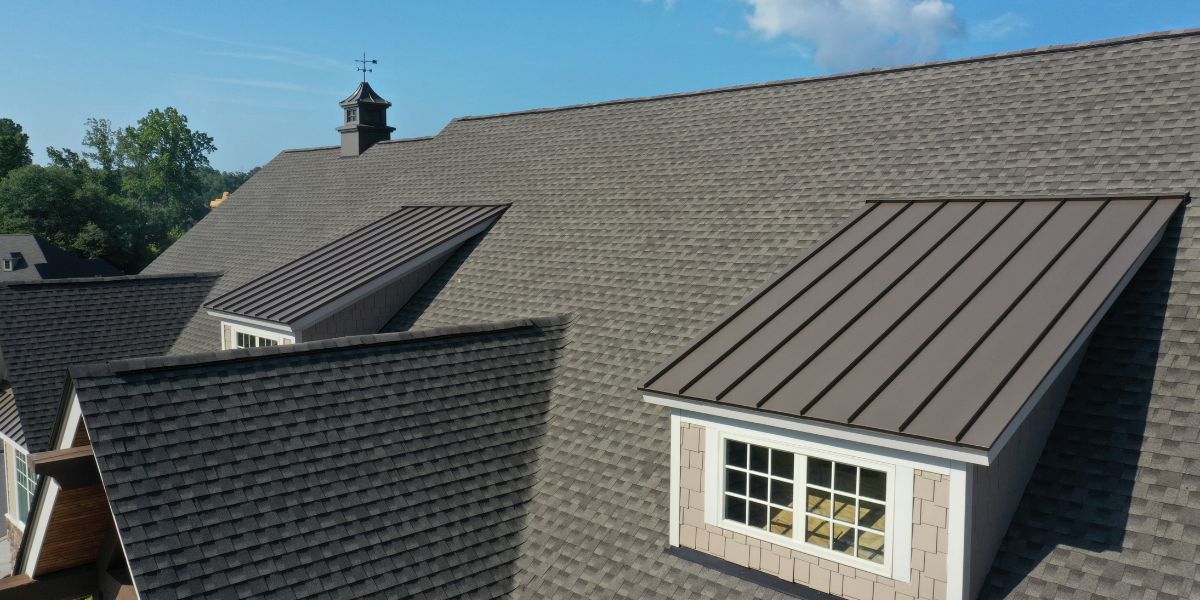 Large roof with a combination of shingles and metal panels, featuring dormer windows and a small cupola on top.