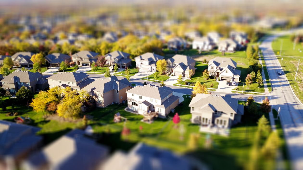 A beautiful modern farmhouse sits atop rolling green hills under a sunny sky, representing the unique and desirable real estate market of Lovettsville.