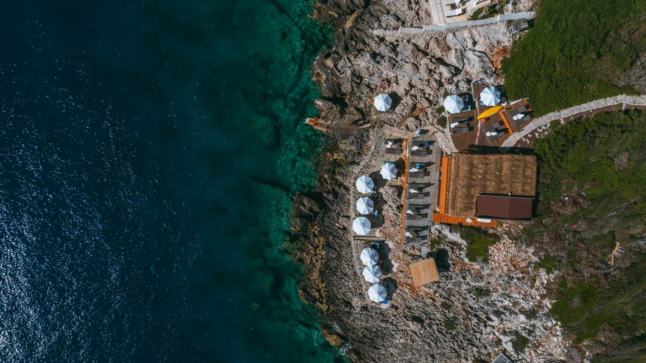 A drone captures an aerial view of a spectacular luxury home situated on a cliff by the ocean, highlighting modern real estate photography and videography technology.